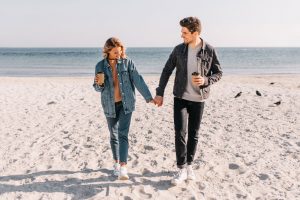 Couple holding hands in PB while holding coffee.